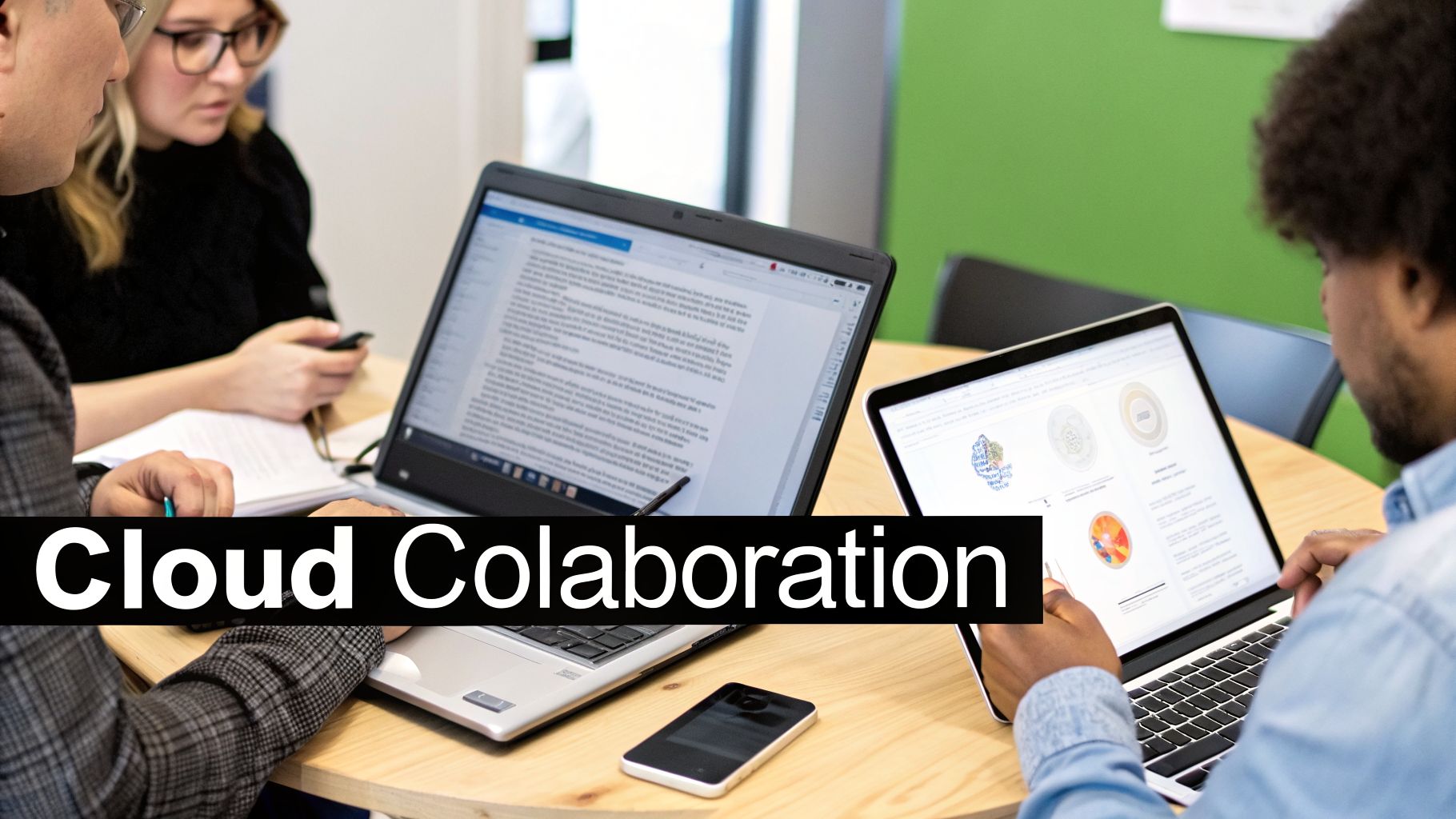 Three professionals are collaborating around a table, working on laptops and using a smartphone for cloud-based tasks.