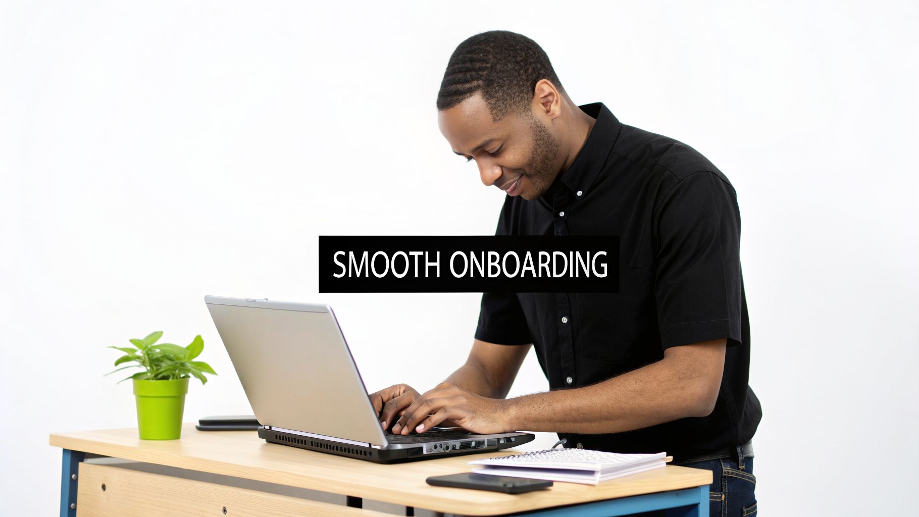 A smiling Black man typing on a laptop at a desk with a plant, symbolizing smooth onboarding.