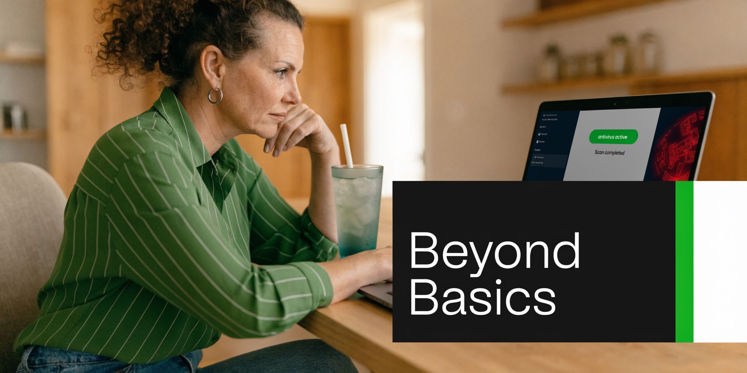 A woman with curly hair working on her laptop with antivirus software running in a home office.